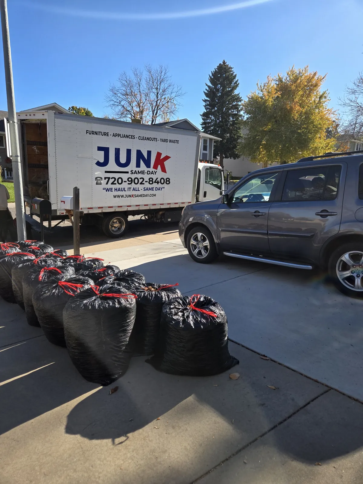 The Junk Same Day 16 ft box truck parked at a Denver driveway with bagged junk loaded out front