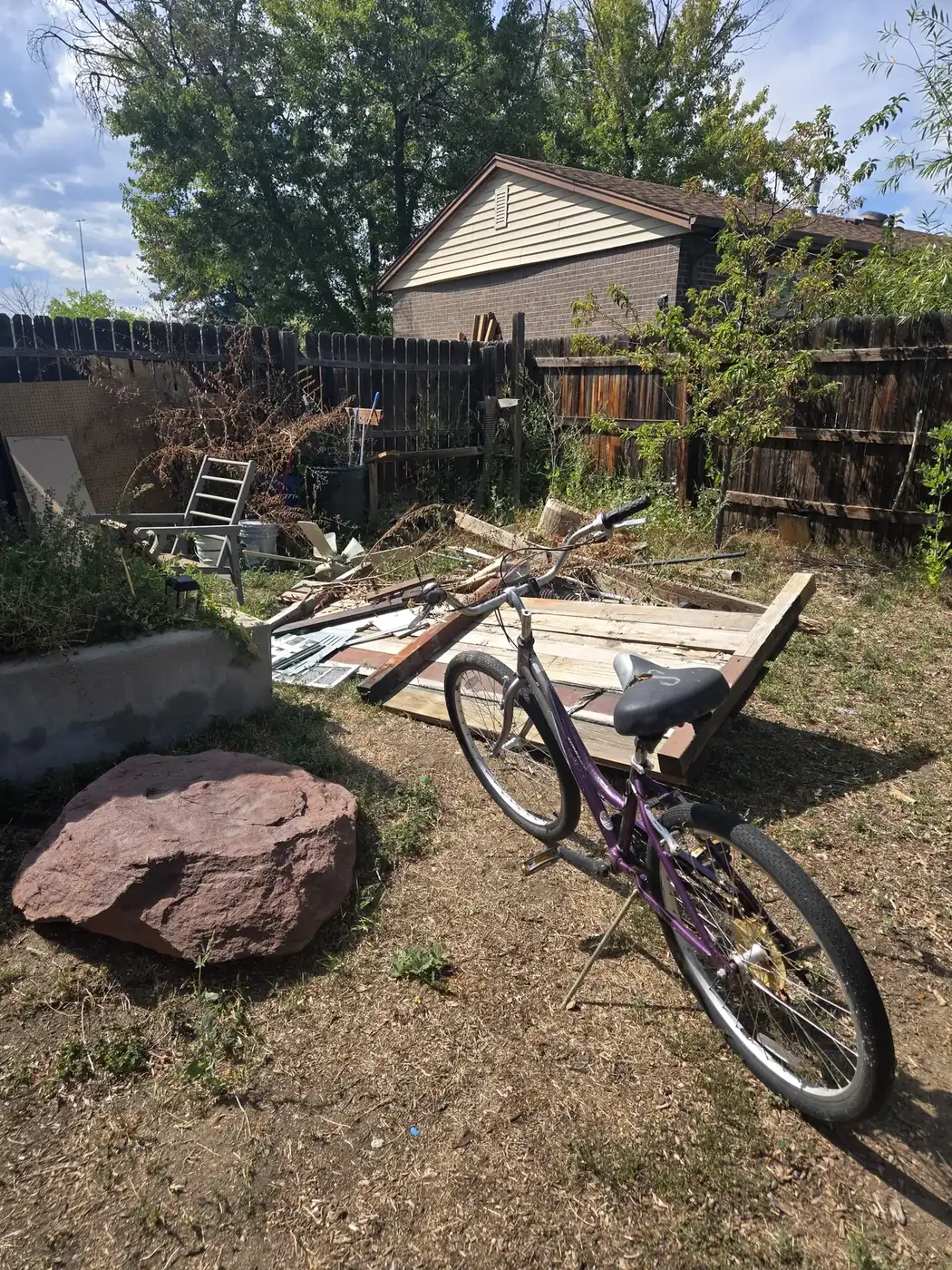 Backyard with debris, lumber and an old bike before cleanup