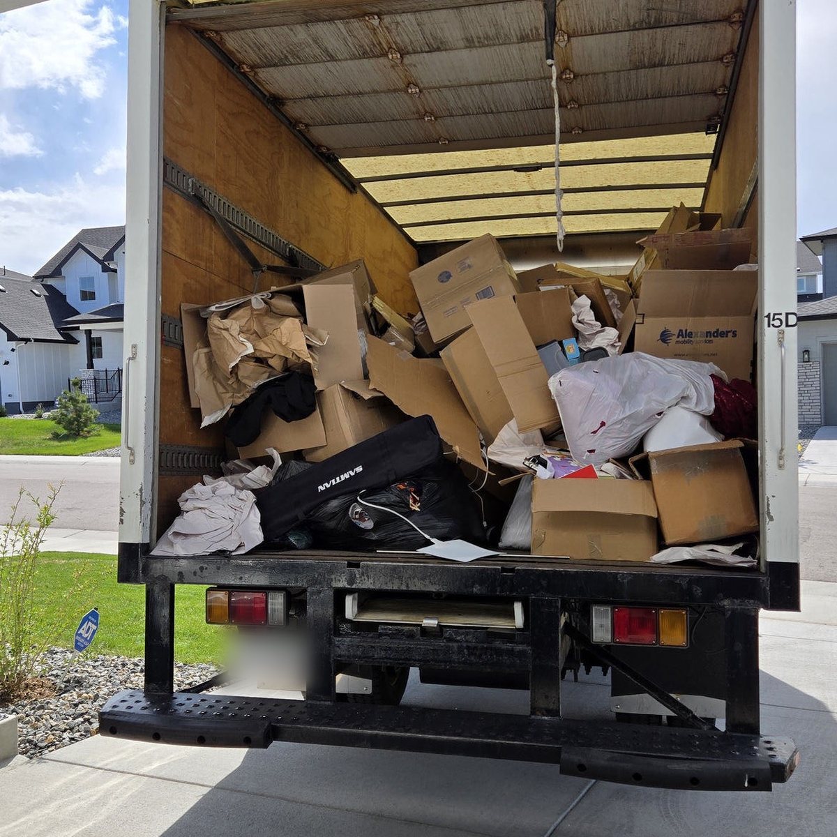 A Junk Same Day box truck loaded with boxes and bagged household waste in a Denver driveway.